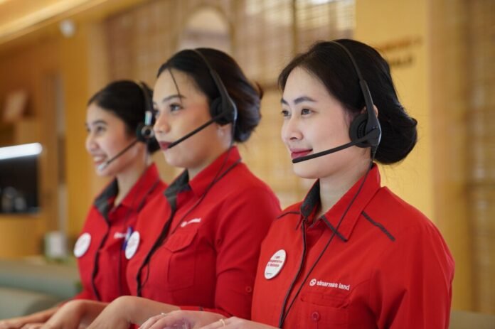 Tiga agen Contact Center Sinar Mas Land mengenakan headset dan seragam merah sedang melayani di Call SML 1500 765, layanan pelanggan properti 24 jam.
