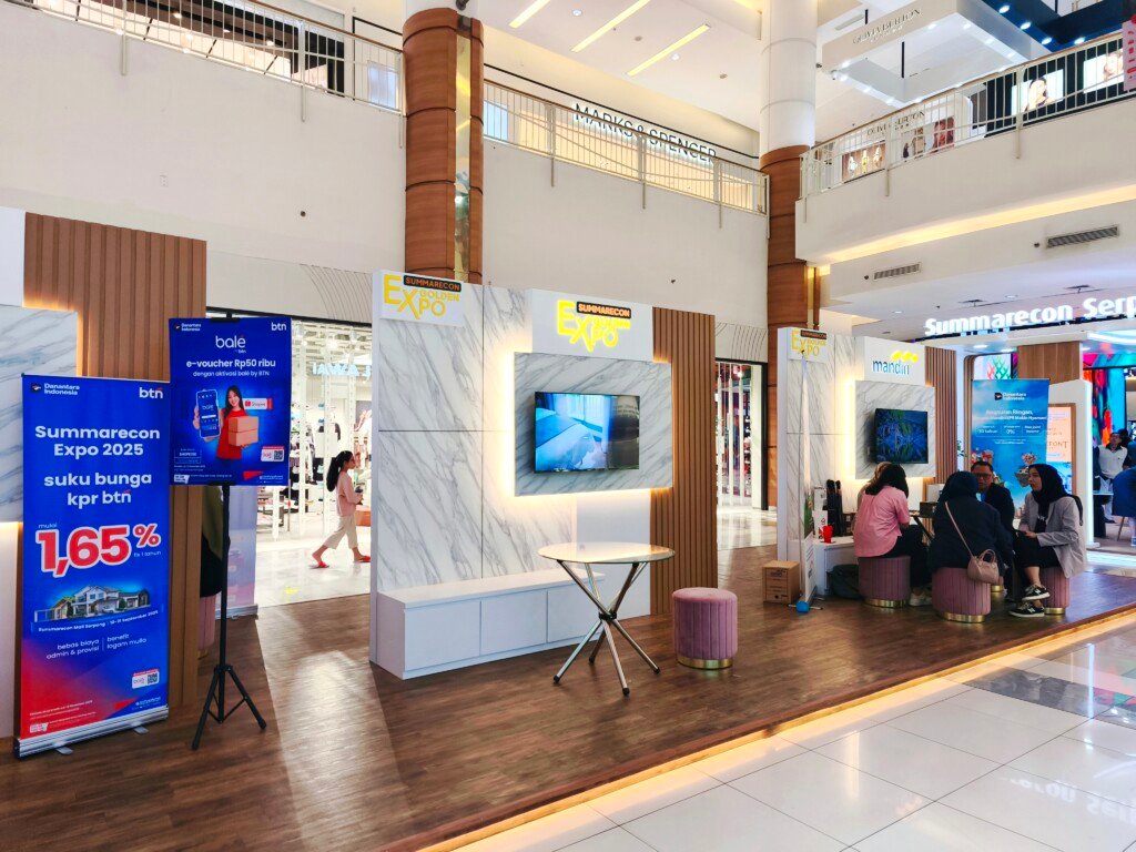 Stan pameran Summarecon Expo 2025 di dalam mal dengan branding Summarecon Serpong, meja kaca bundar, dan bangku berwarna pink. Terlihat juga spanduk bank BTN yang menawarkan suku bunga KPR 1.65% untuk acara ini.