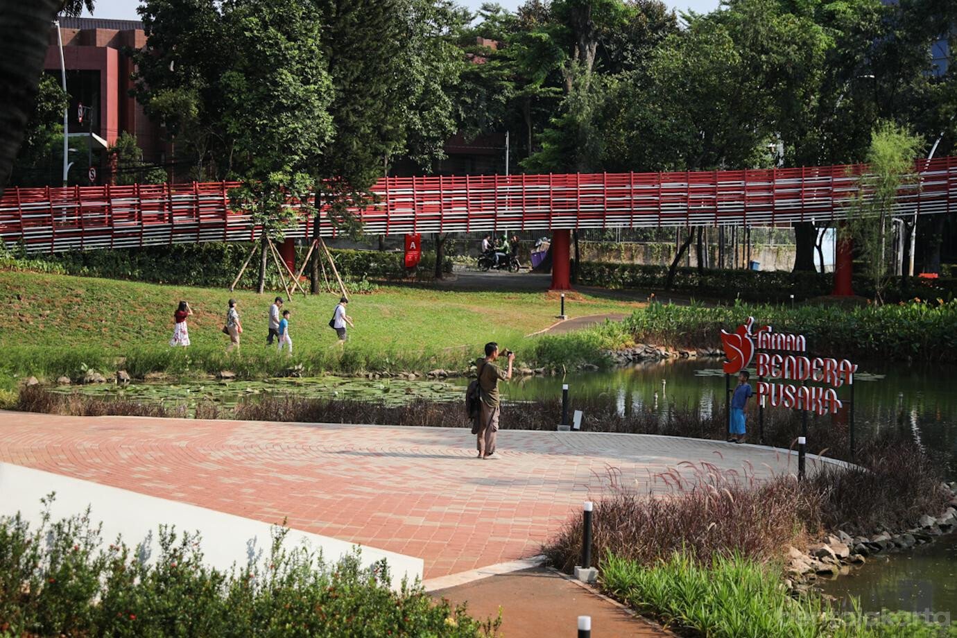Suasana danau buatan dan jembatan merah putih di Taman Bendera Pusaka Kebayoran Baru, rekomendasi taman kota di Jakarta yang hits untuk nongkrong.