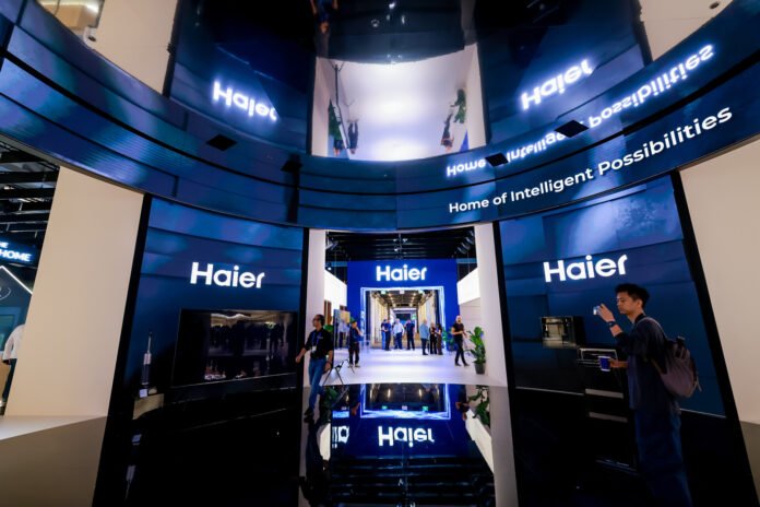 Suasana stan pameran Haier di IFA 2026 yang menampilkan panggung futuristik dengan layar lengkung bertuliskan Home of Intelligent Possibilities dan logo Haier untuk memamerkan teknologi smart home AI.