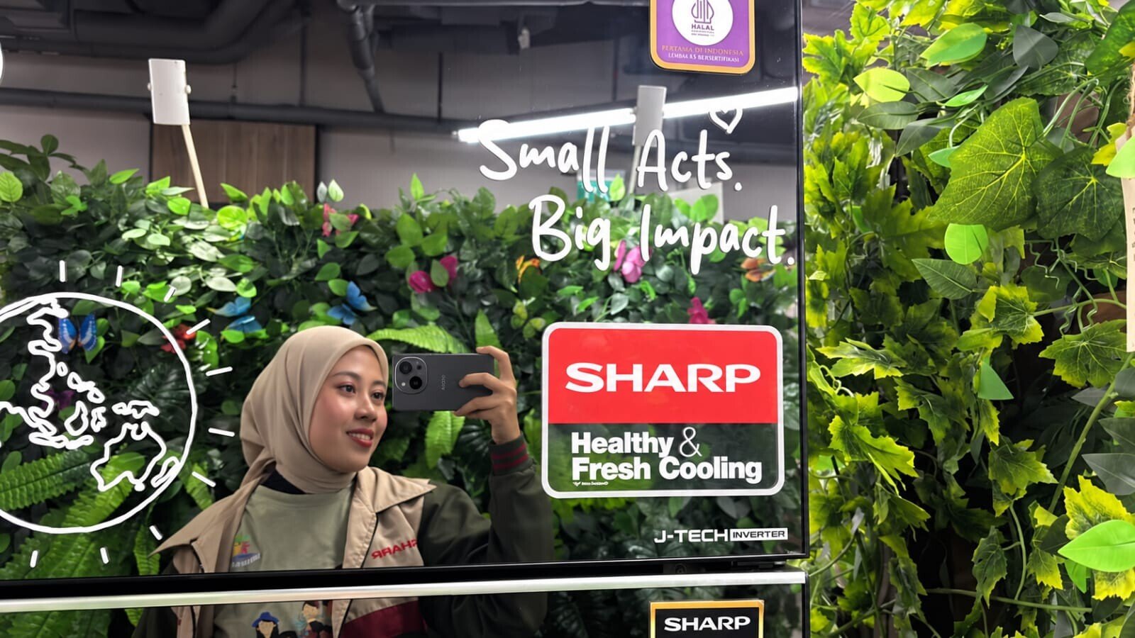 Anggota Sharp Greenerator melakukan mirror selfie pada refleksi pintu lemari es Sharp bersertifikasi hemat energi di area Langkah Membumi 2026.